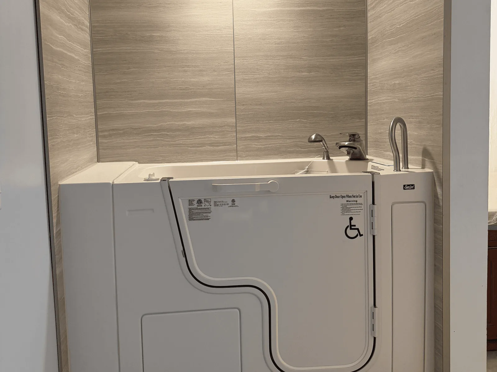 Accessibility remodeling: a walk in tub with a low entry door and a handheld shower installed in a tiled alcove