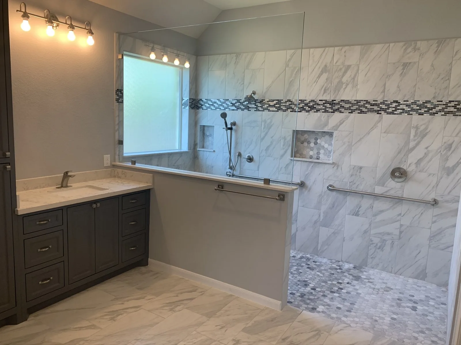 Accessibility remodeling: a zero entry tiled shower with grab bars and a handheld shower beside a dark vanity