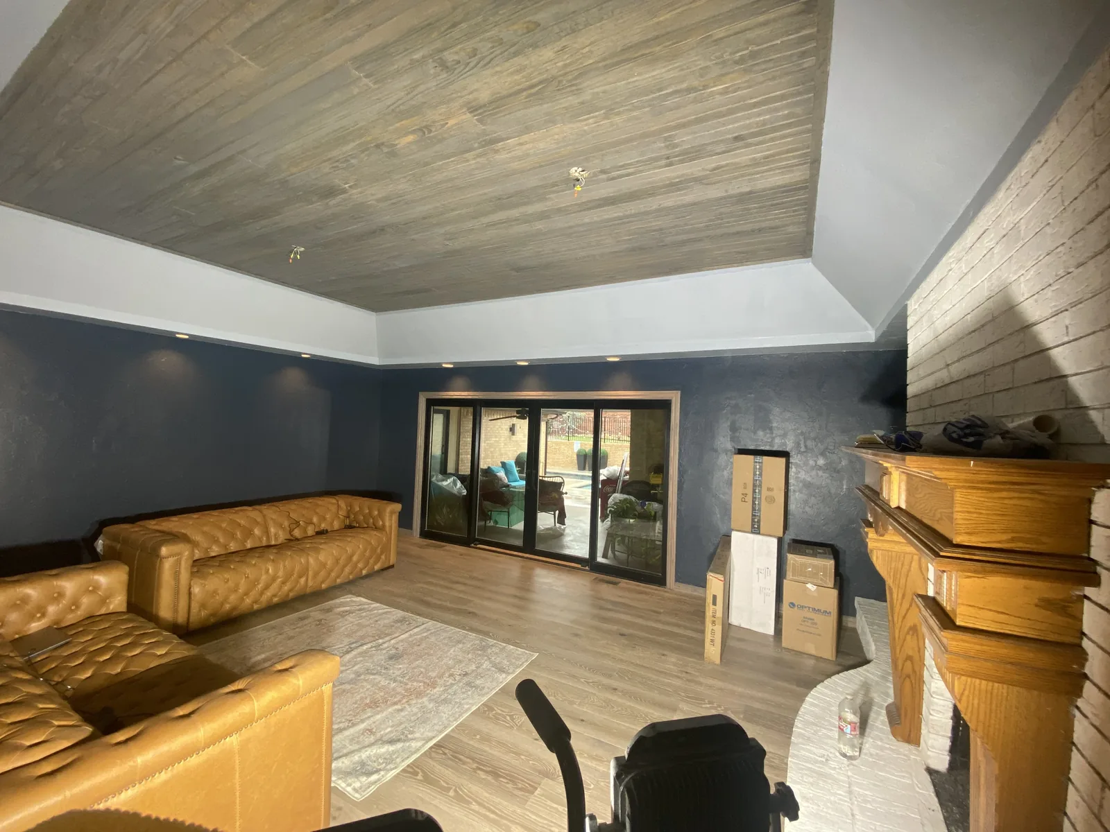 Home remodeling: a living room with a new wood plank tray ceiling, navy walls, a brick fireplace and sliding doors to the patio