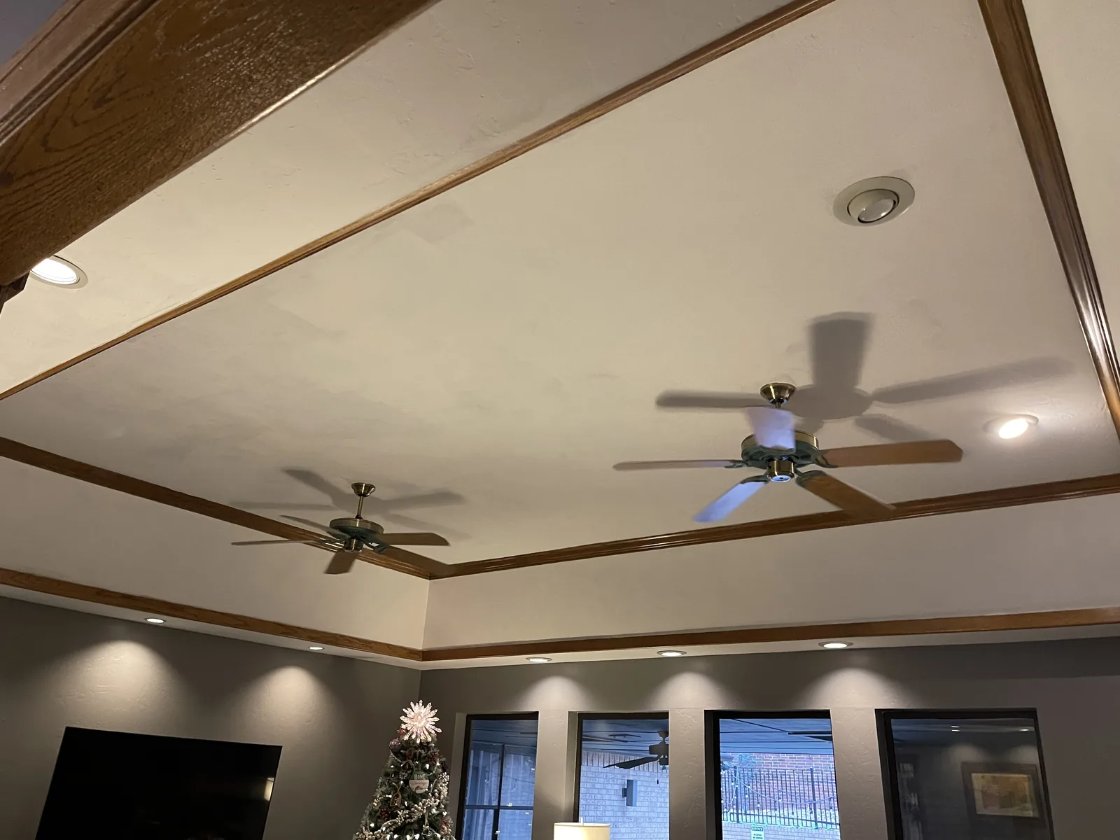 Living room before the remodel: a flat tray ceiling with wood trim, two ceiling fans and recessed lights