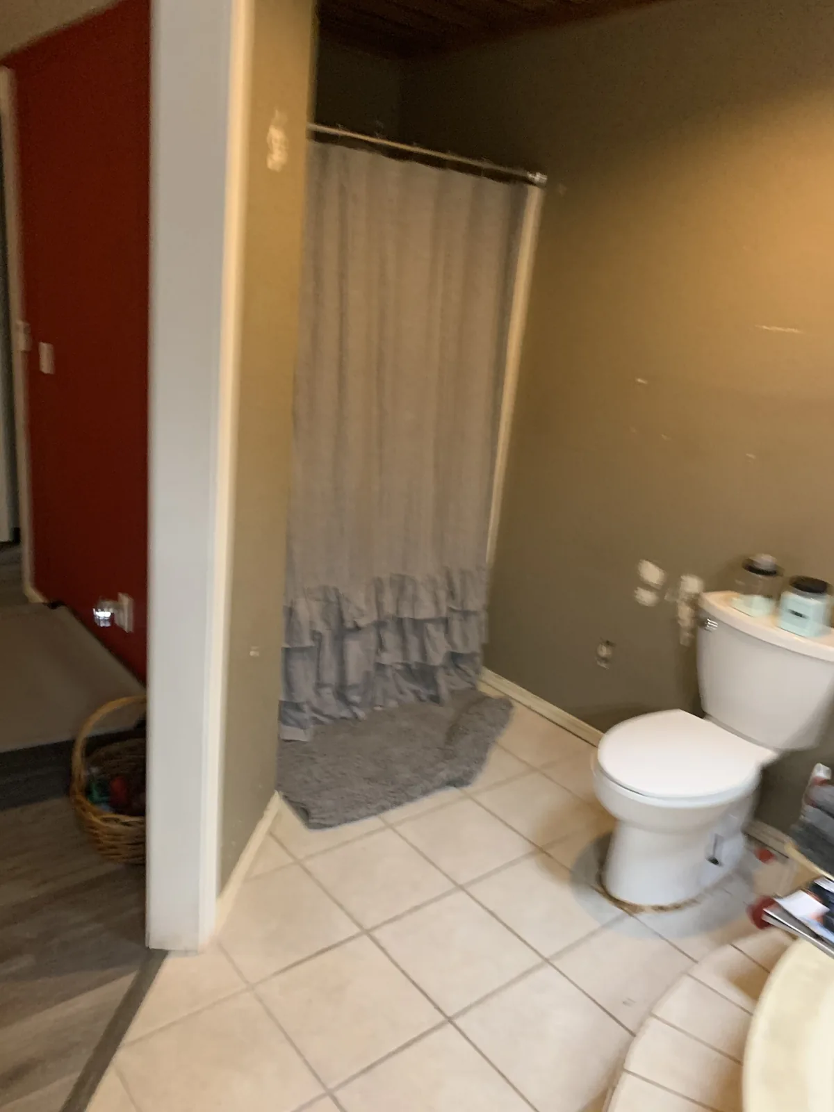 Bathroom before the remodel: a corner shower behind a curtain, a toilet and a cream tile floor
