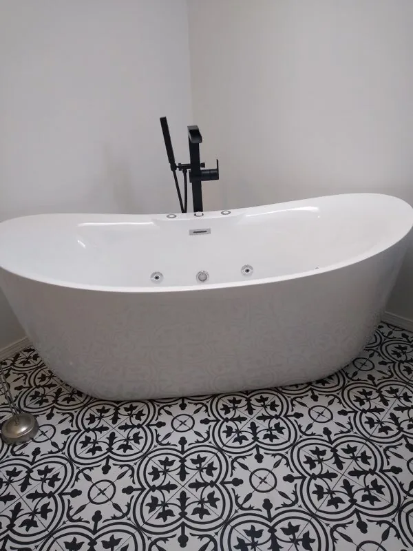 Bathroom remodeling: a white freestanding tub with a black floor mount faucet on a black and white patterned tile floor