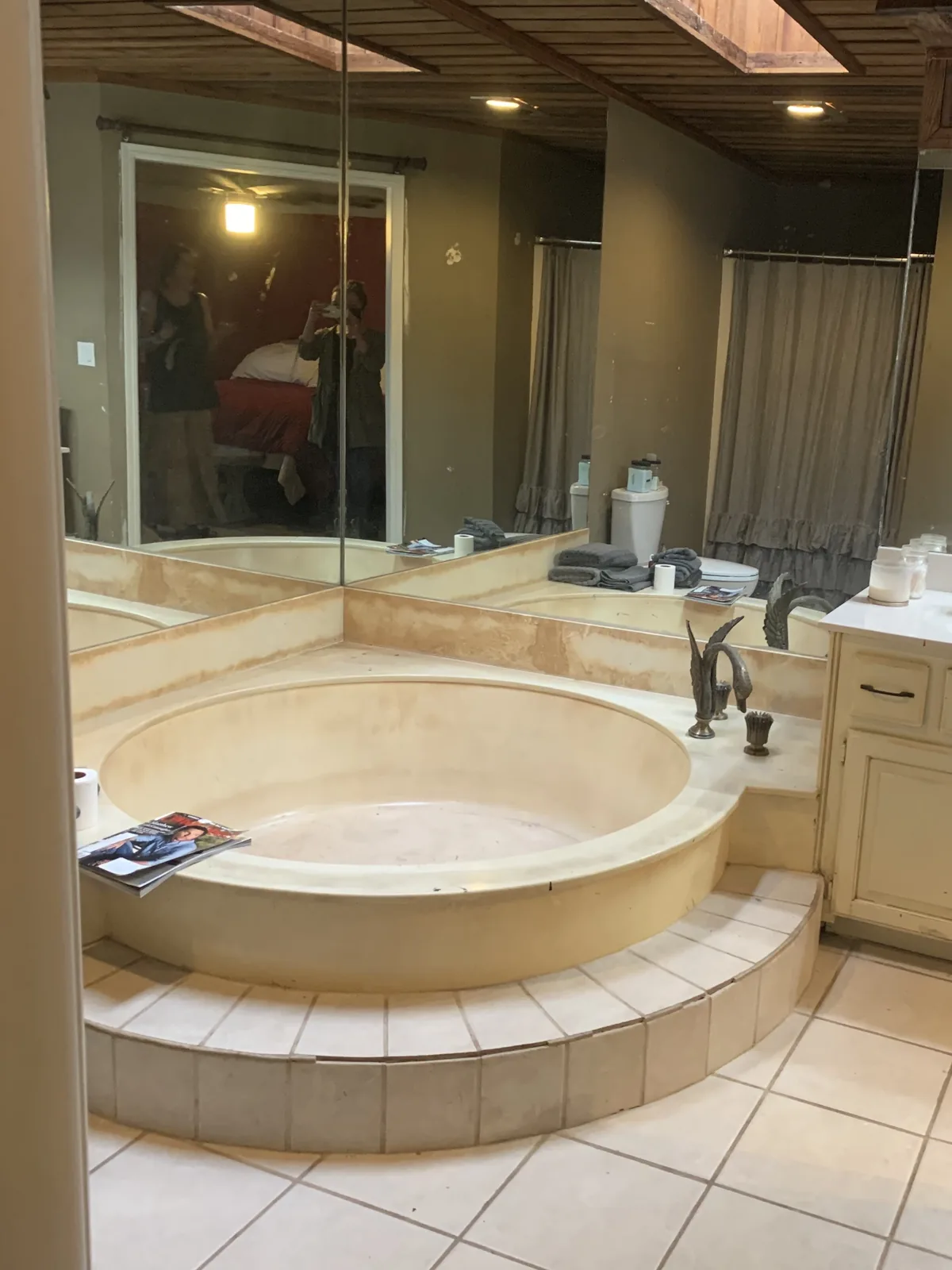 Master bathroom before the remodel: a round sunken tub on a raised tile platform with mirrored walls and a cream vanity