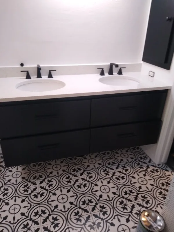 Bathroom remodeling: a black double vanity with a white quartz top, black faucets and a patterned tile floor
