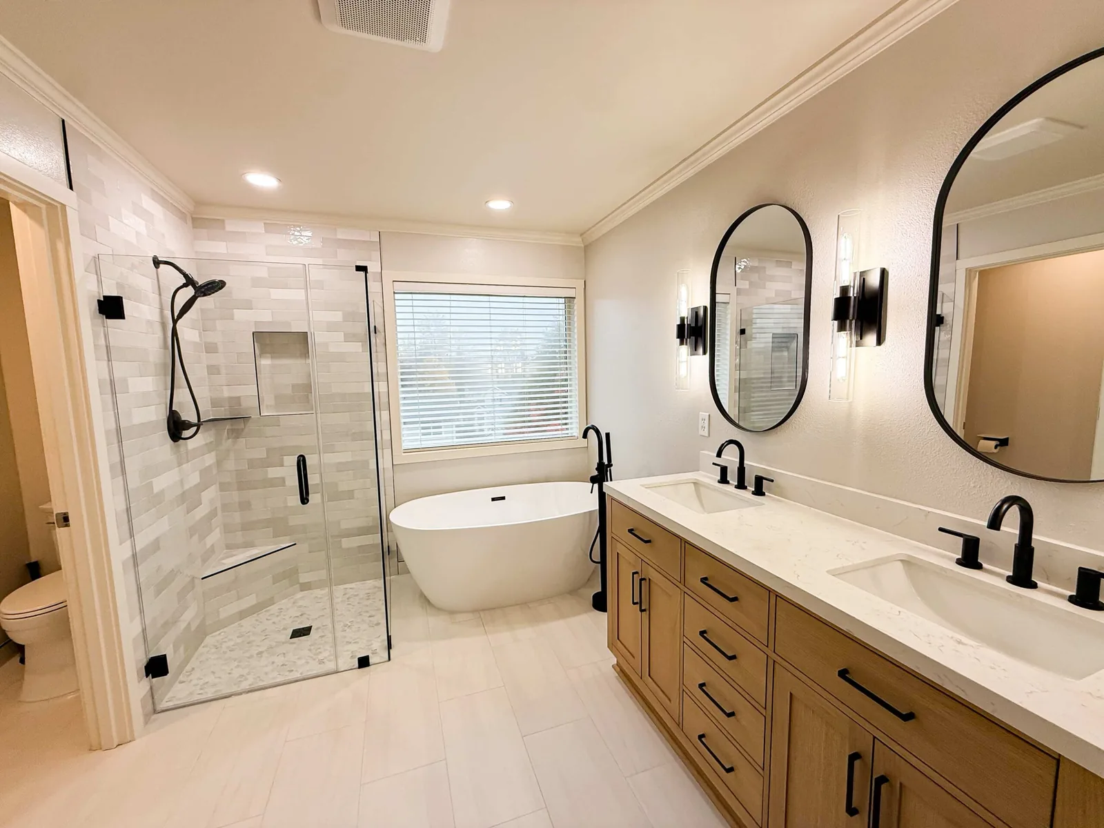 Bathroom remodeling with a glass tile shower, a freestanding tub and a wood double vanity with black fixtures