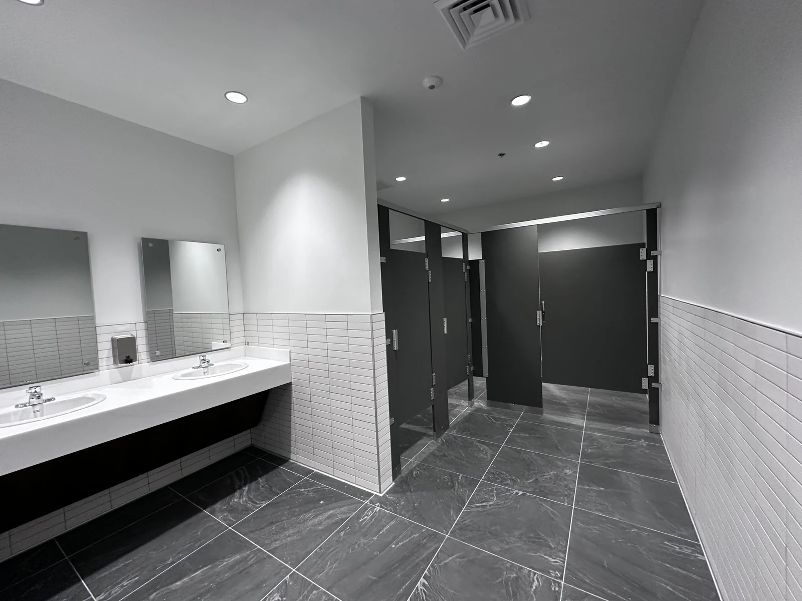 Commercial remodeling: a finished restroom with a tiled wainscot, a two sink vanity counter and black stall partitions