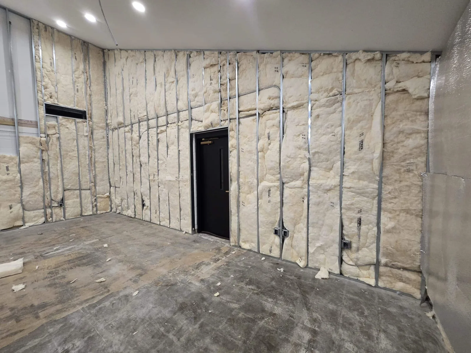 Commercial remodeling in progress: metal stud walls packed with insulation and electrical boxes in a small commercial room