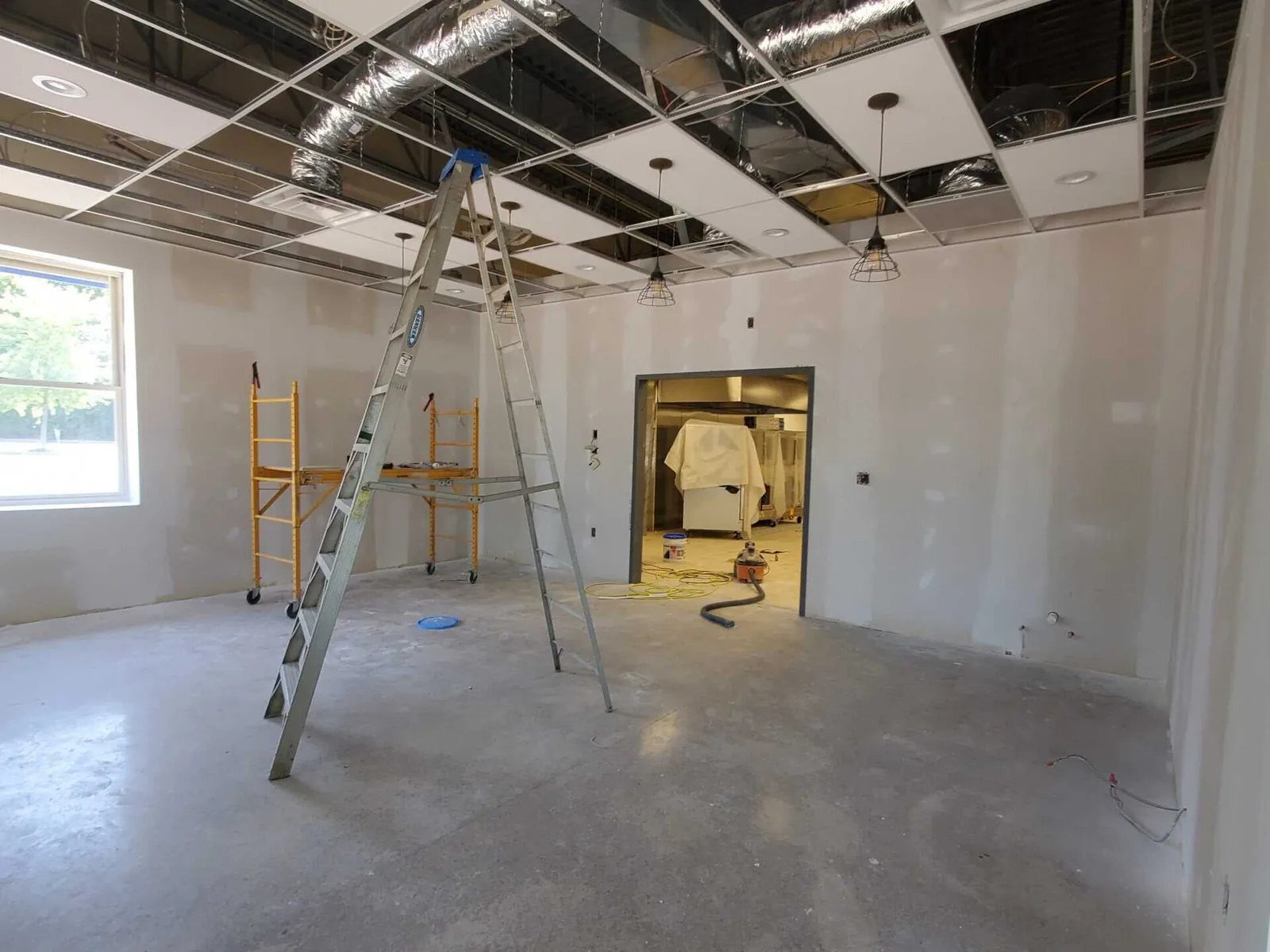 Commercial remodeling in progress: a small storefront space with new drywall, a ceiling grid going in and a ladder