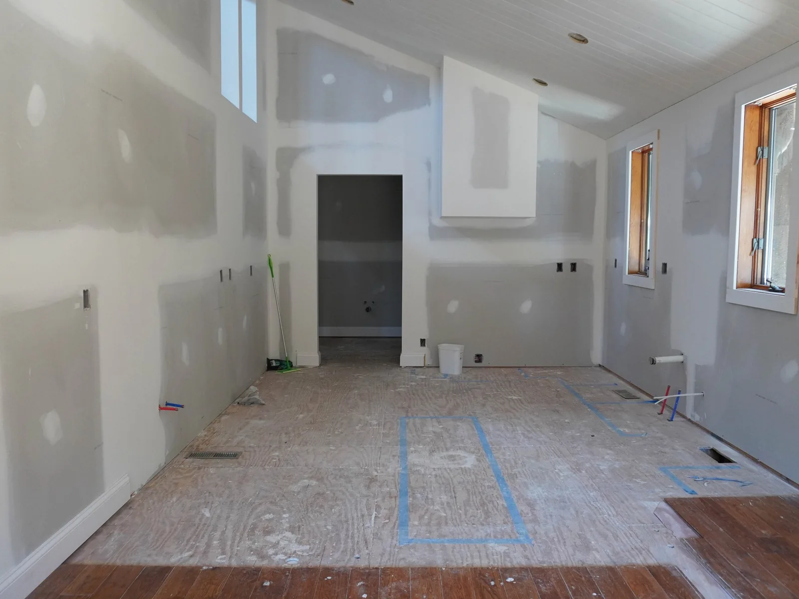 Home remodeling in progress: new drywall hung and taped over a bare plywood subfloor marked out in blue tape