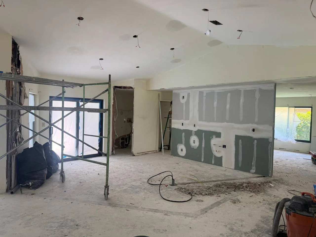 Home remodeling in progress: an opened up interior with a new drywall wall being taped, scaffolding and recessed light cutouts
