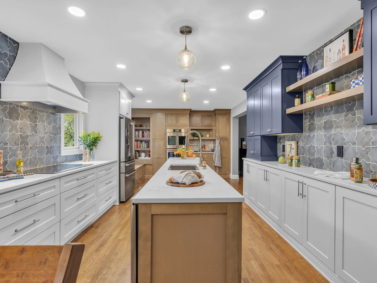 Kitchen remodeling with white and navy cabinets, a gray patterned tile backsplash, a white range hood and a long island