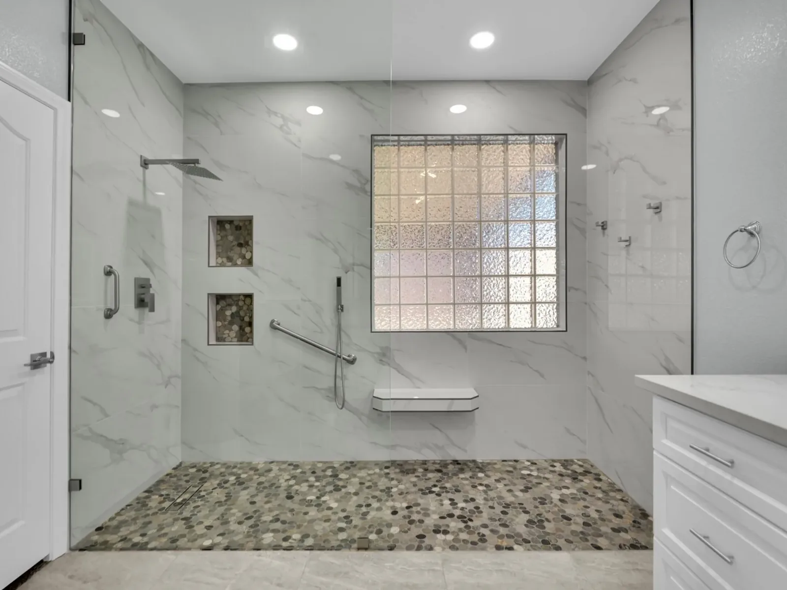 Shower remodel with a curbless walk in shower, a pebble tile floor, a grab bar and a fold down seat
