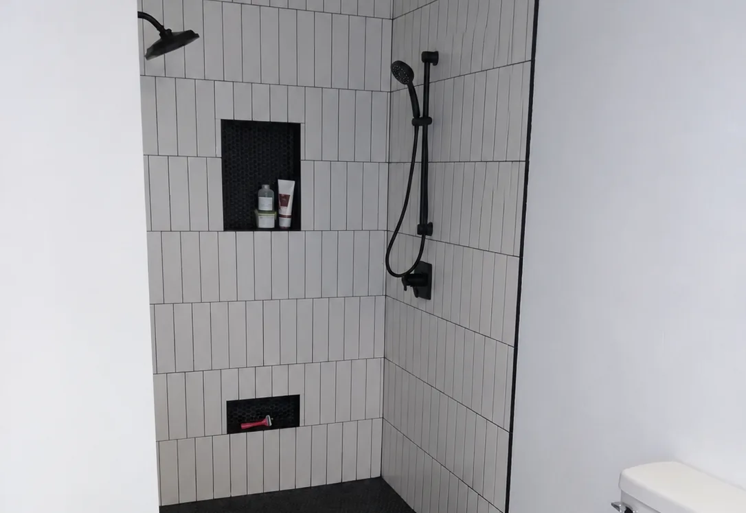 Shower remodeling: a walk in shower with white vertical subway tile, black fixtures and two tiled niches