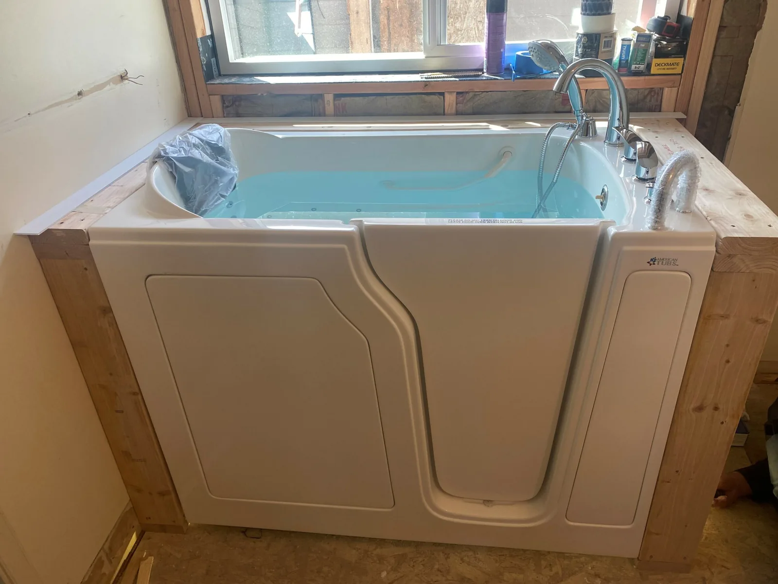 Walk in tubs: a walk in tub being installed, set in a new wood frame under a window before the surround goes on